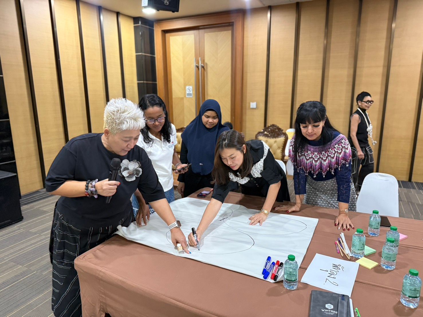 Diverse group of five people collaborating on a large paper on a table.