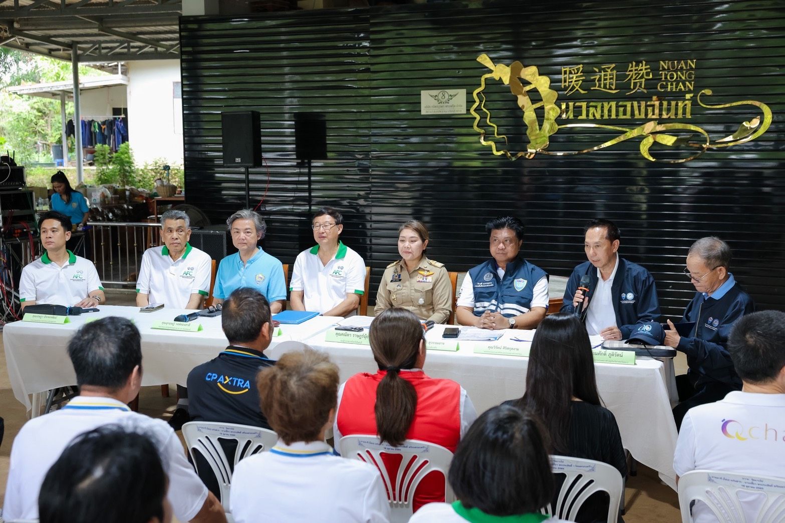 Seven officials sit at a table addressing an audience at a community event.