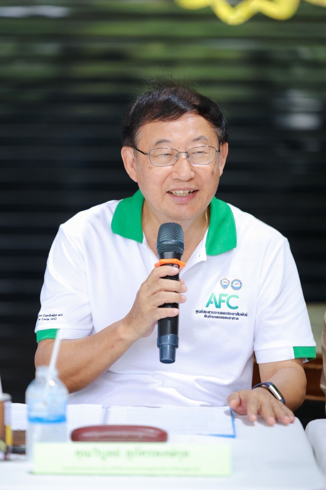 Man in glasses speaking into a microphone, wearing a white polo shirt with a PPC logo.