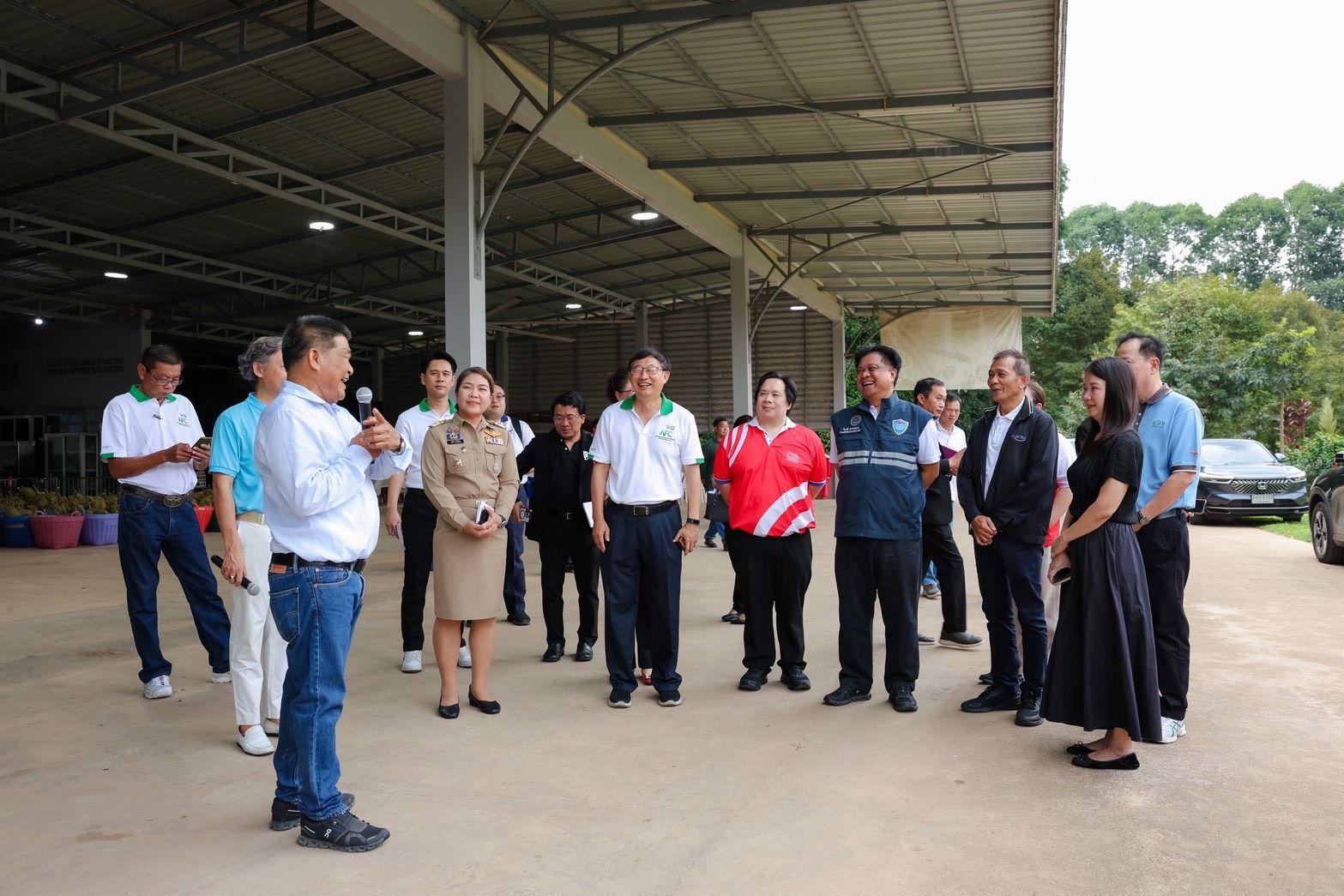 A man speaks into a microphone, addressing a group of officials and workers inside a large facility.
