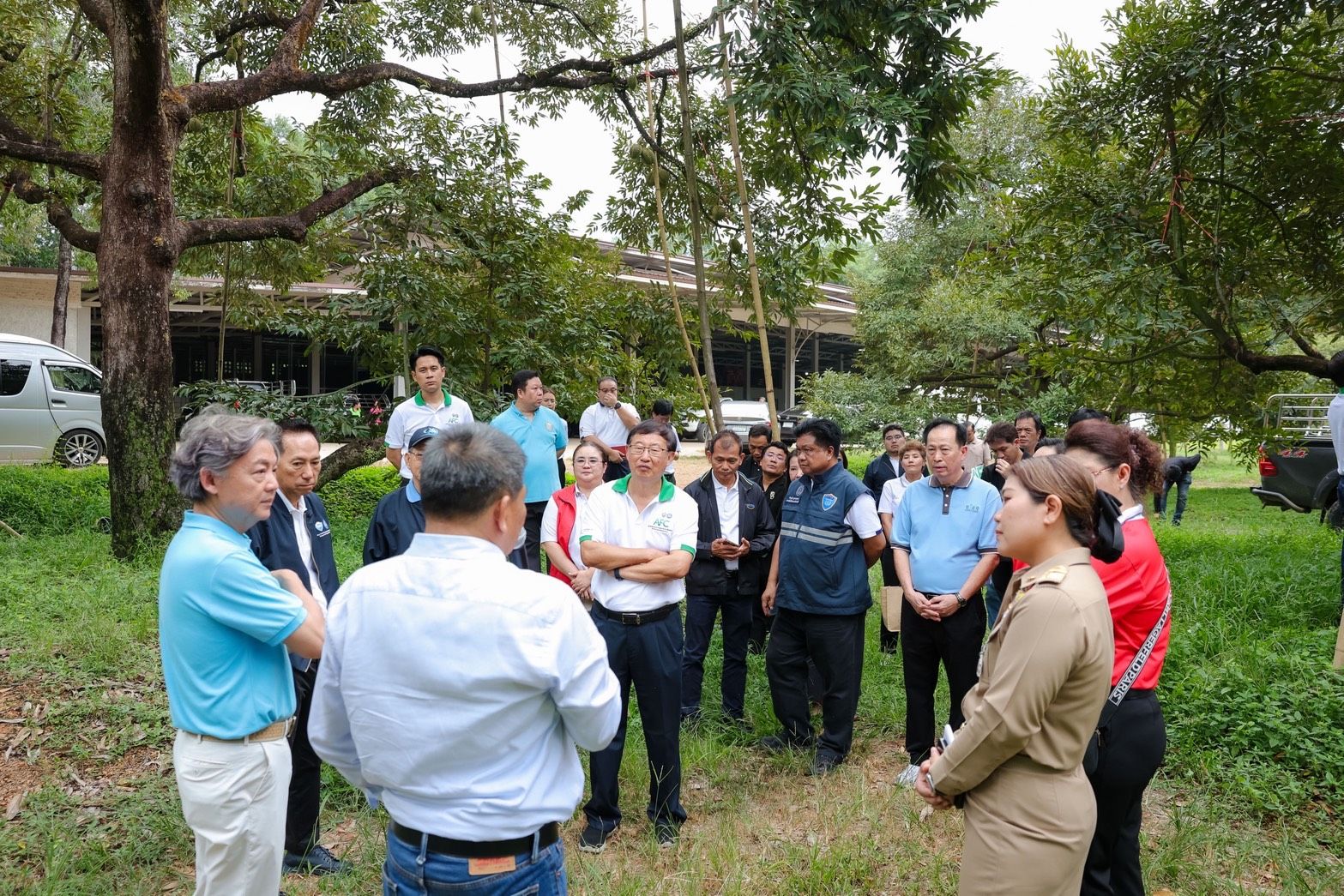 A diverse group of professionals meets outdoors among trees for a discussion.