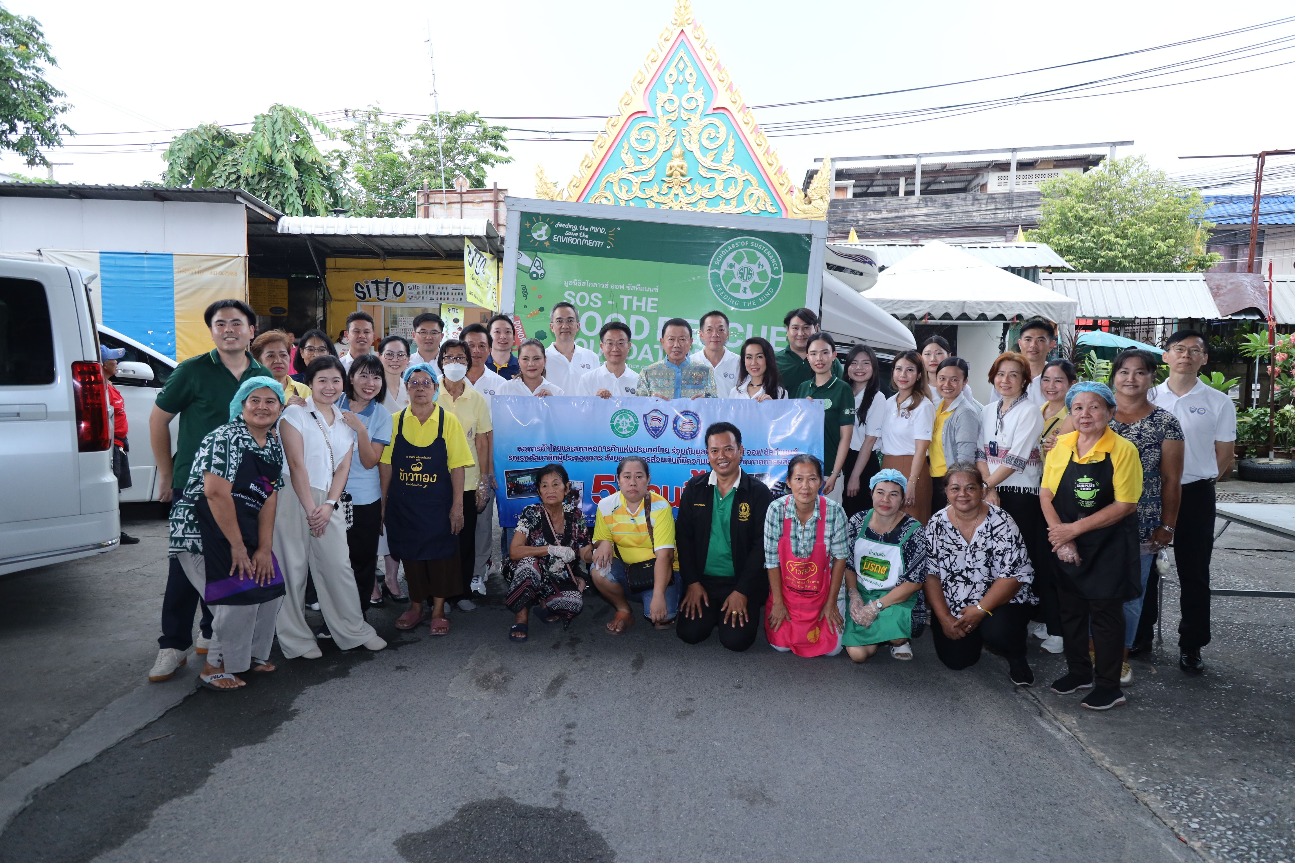 A large group of people, some holding a banner, gather for a community event outdoors.