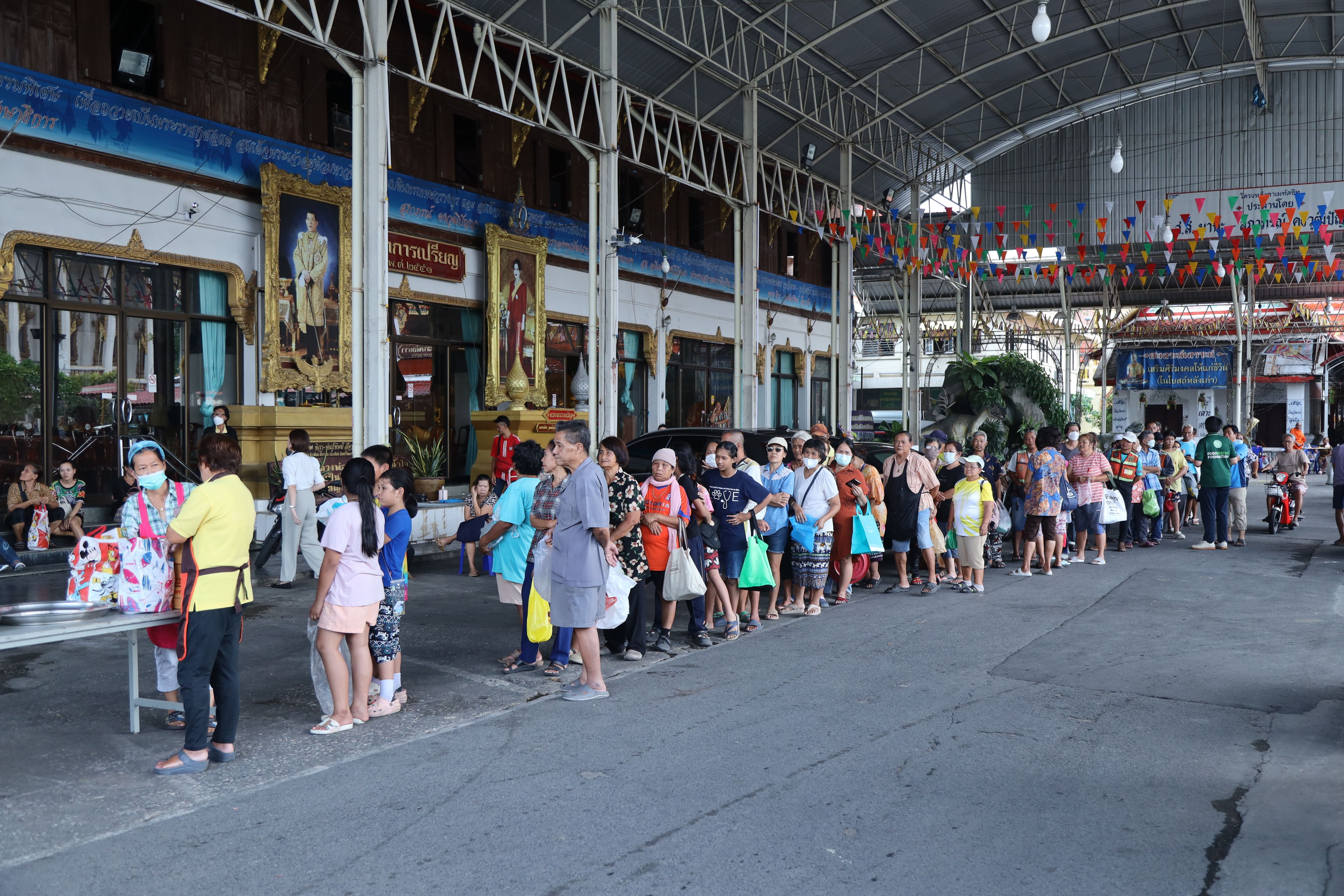 A line of people waits patiently for food distribution at an outdoor community event.