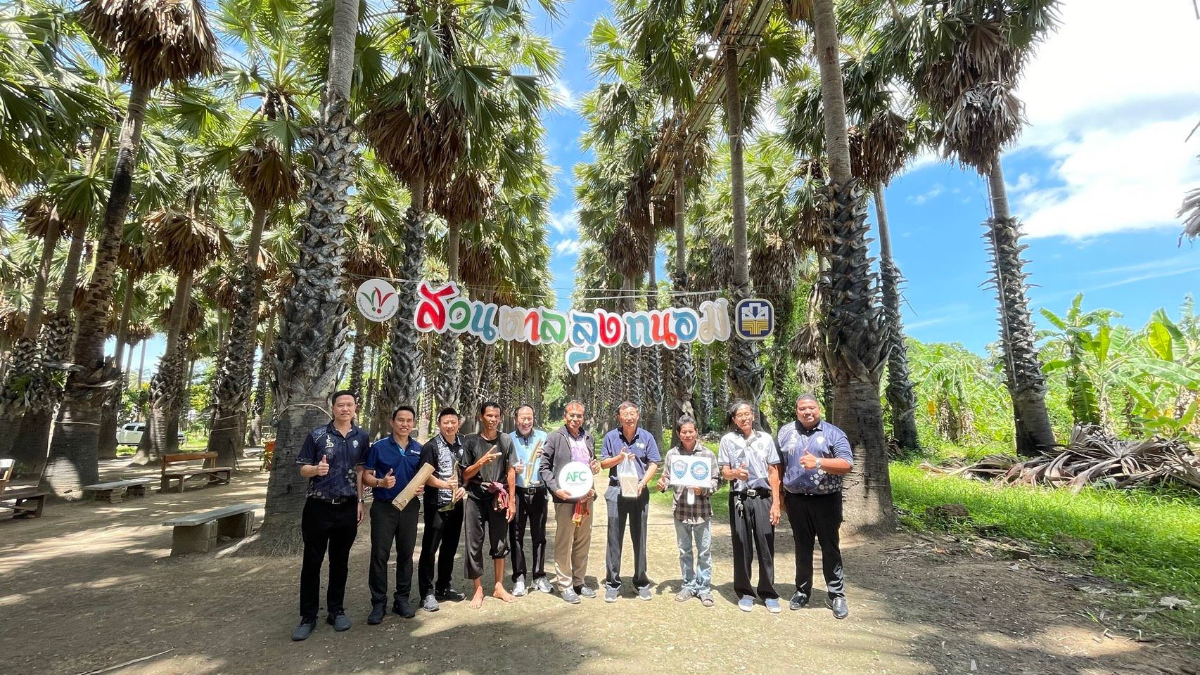 Group of people standing under a banner on a path lined with tall palm trees.