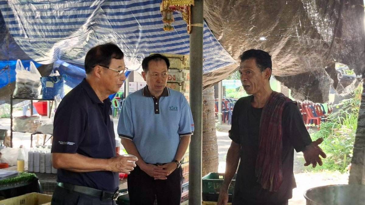 Three men discuss under a shaded outdoor market stall, one gesturing passionately.