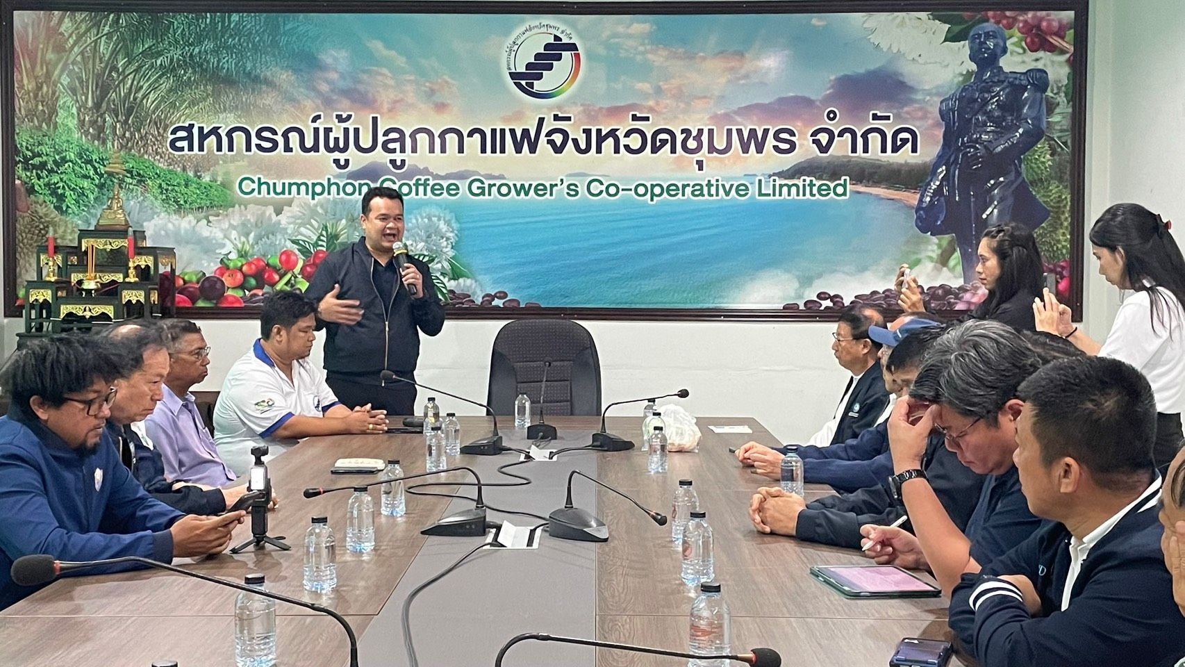 Man speaking to a group of men at a conference table with a cooperative banner.