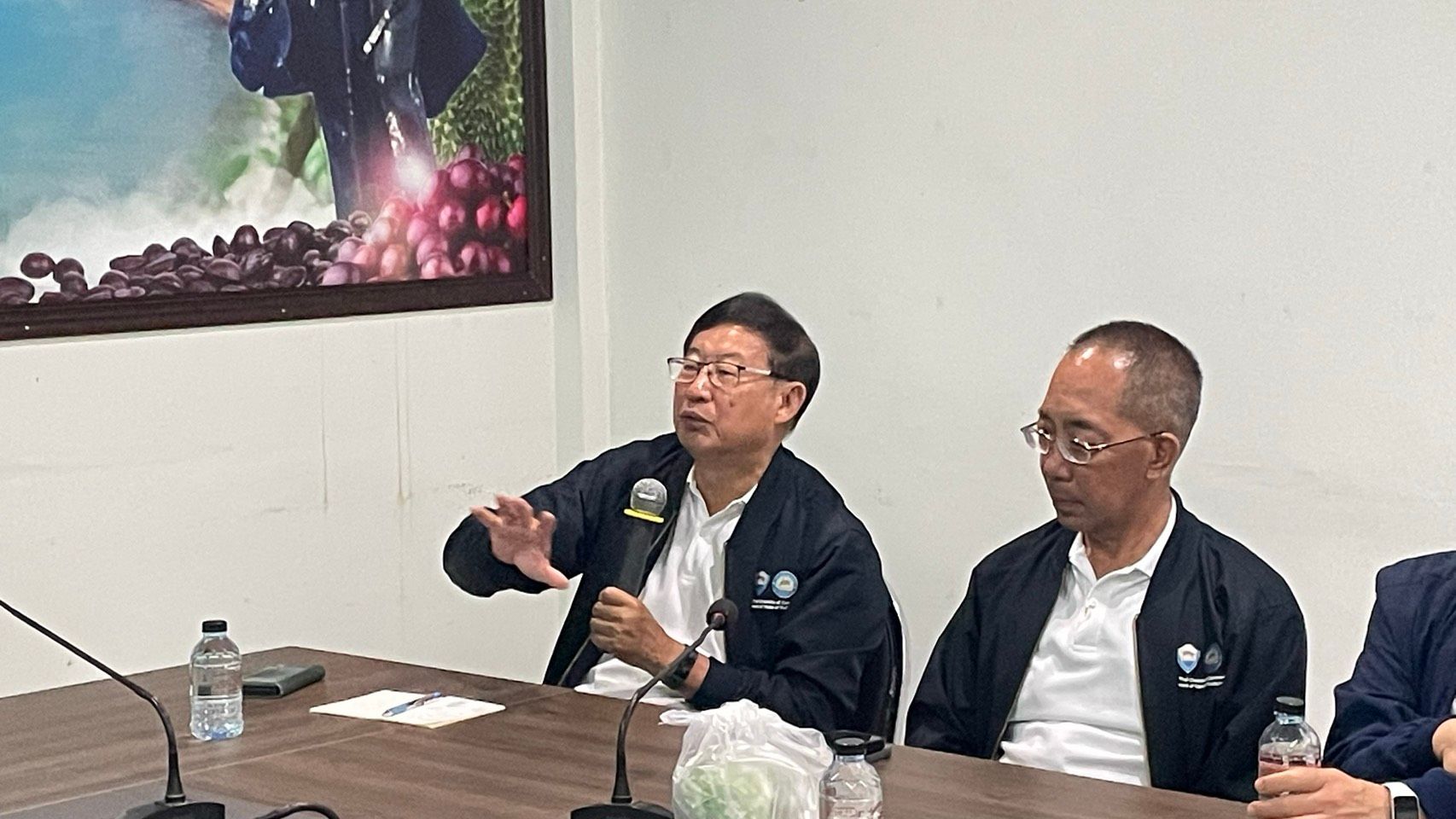 Man in glasses gestures while speaking at a table with another man.