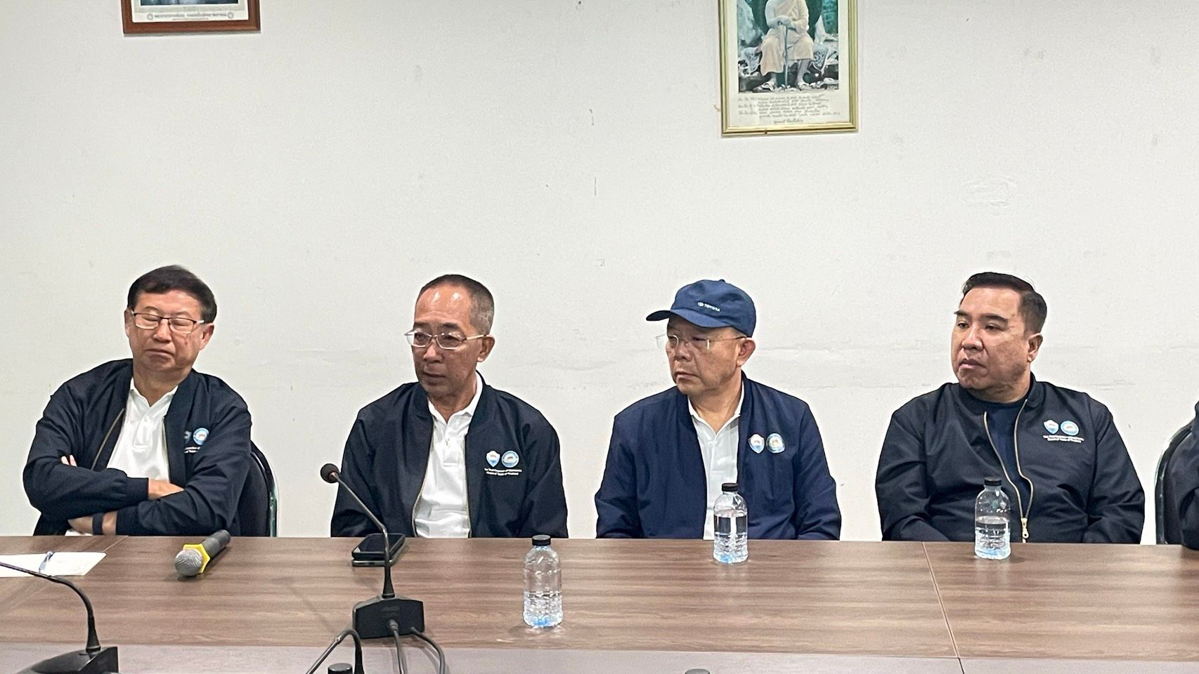 Four Asian men in dark jackets sit attentively at a conference table.
