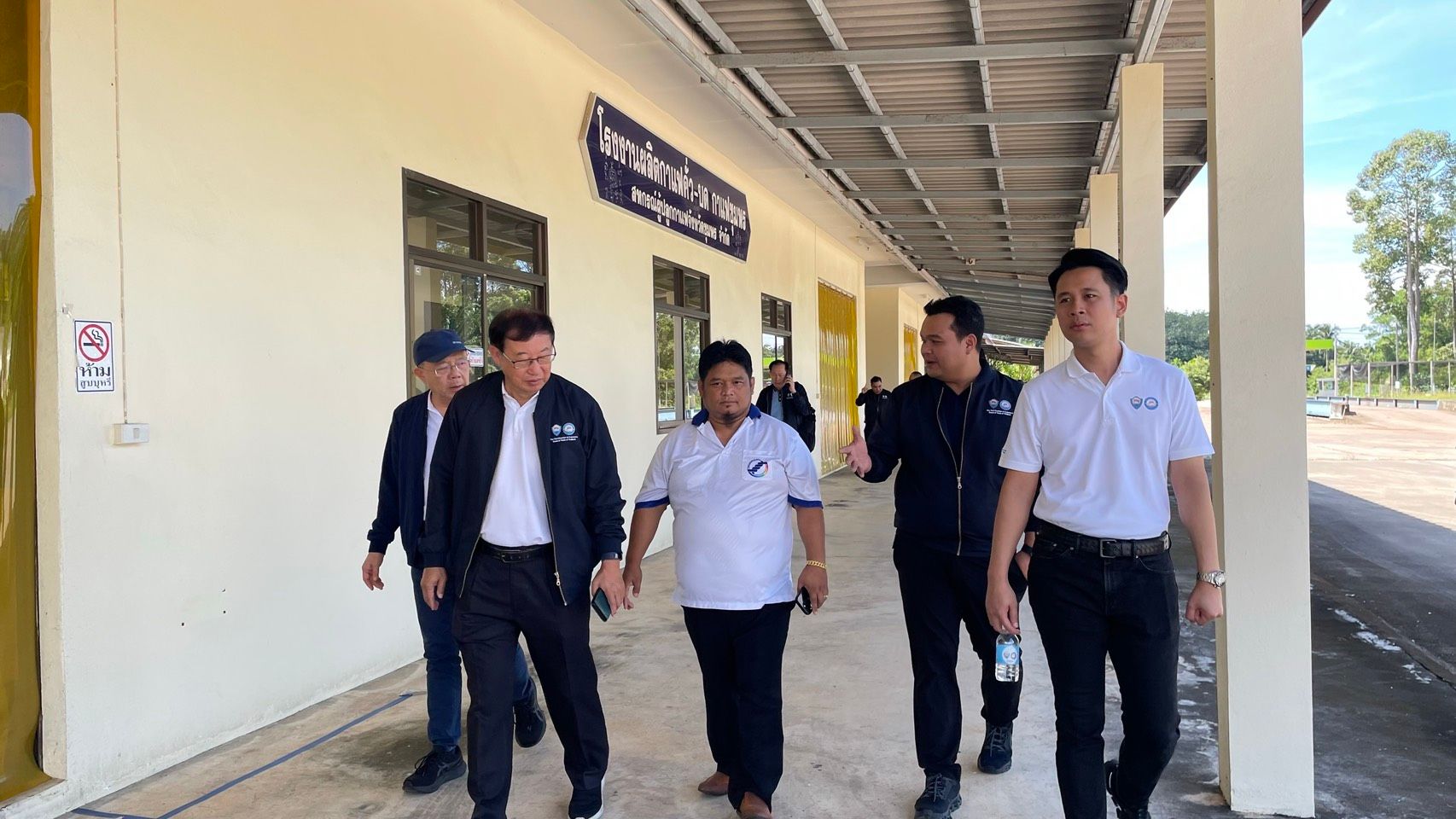 Five men in business casual attire walk along a covered outdoor walkway beside a building.