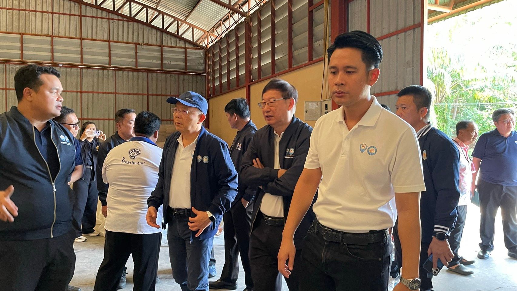 Men in casual attire gather in a large warehouse for an inspection or meeting.