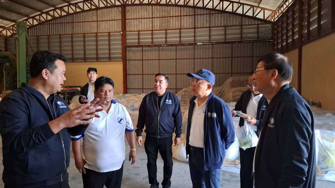 A group of men discusses inside a large warehouse with stacked sacks of goods.