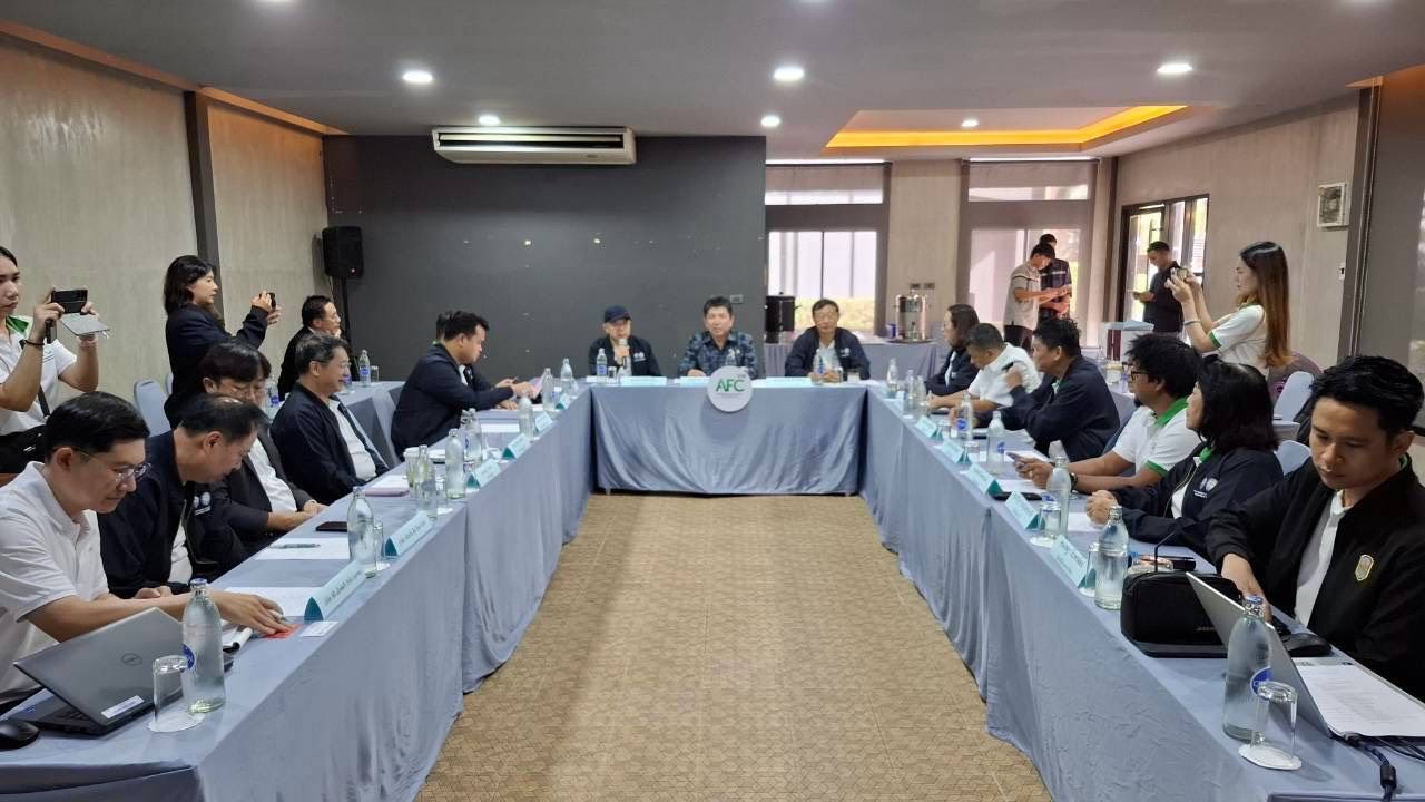 People attending a formal meeting around a U-shaped table in a bright conference room.