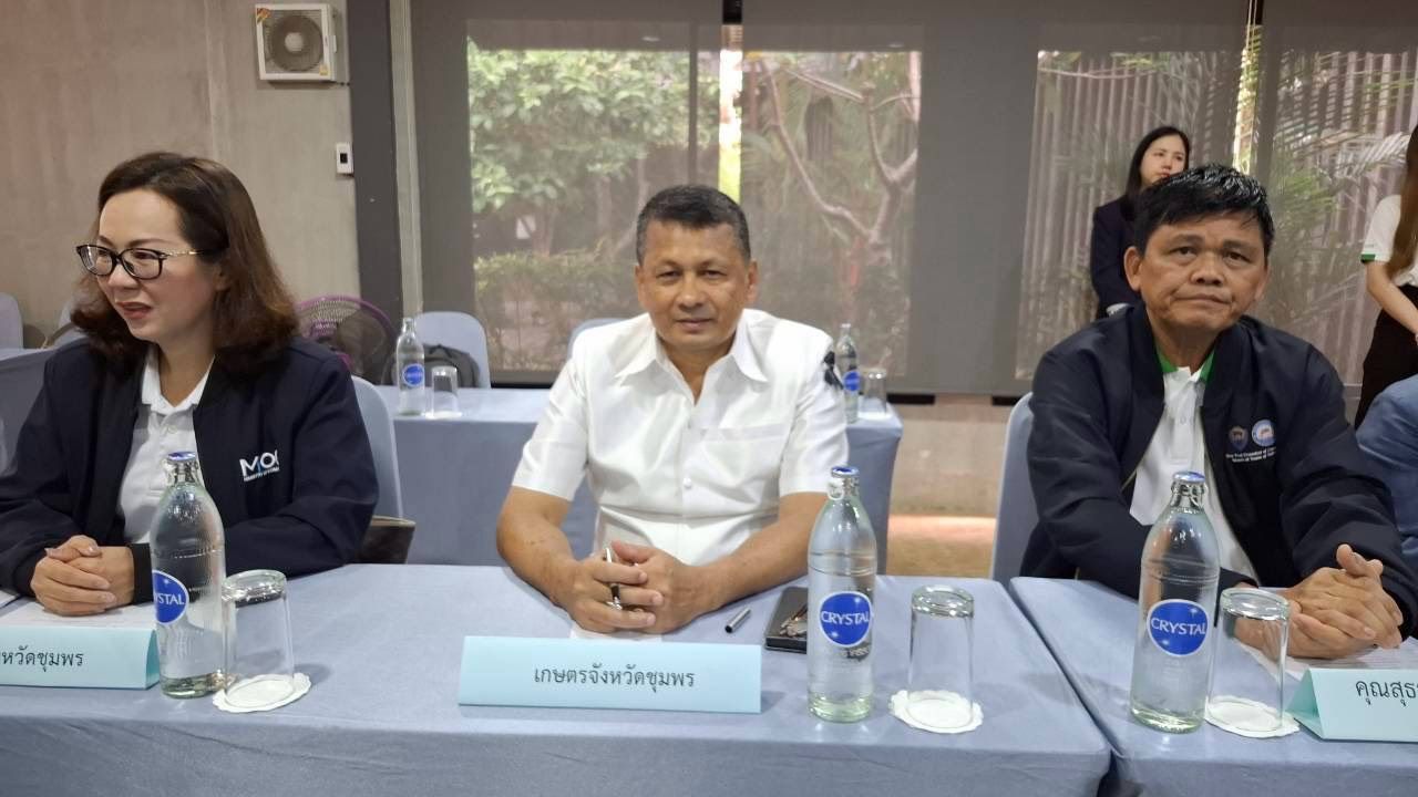 Three people sit at a conference table with water bottles, attending a meeting.