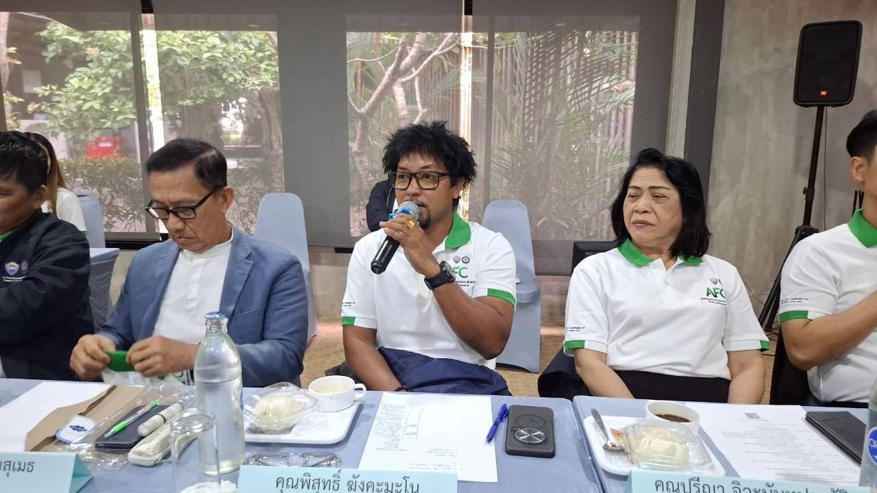 Man with curly hair speaks into microphone at a table with two colleagues.