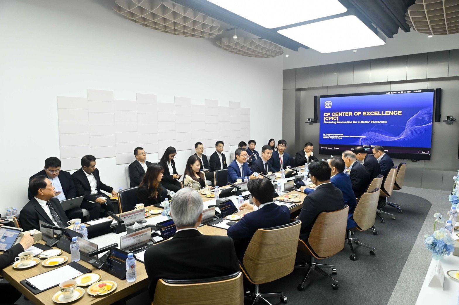 Professionals in a modern conference room attend a meeting with "Recognition of Excellence" displayed on screen.