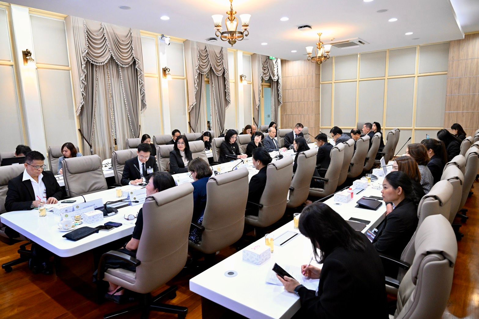 Formal meeting with many people seated around a large conference table.
