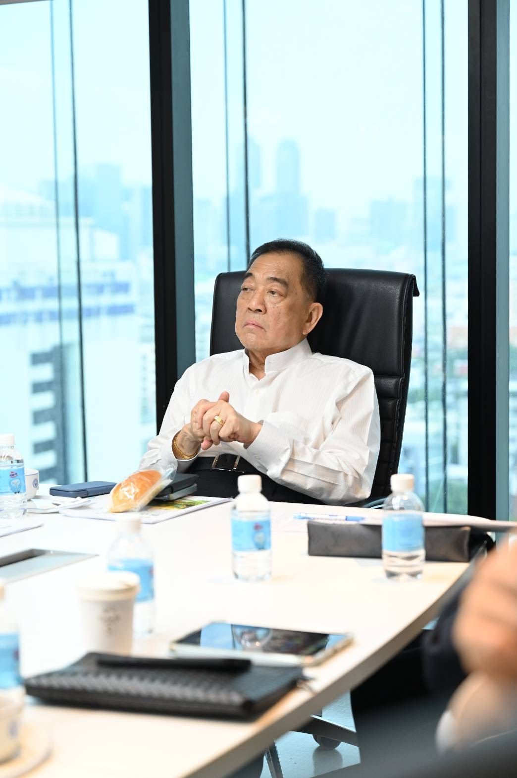 Man in white shirt seated at conference table in modern office with city view.
