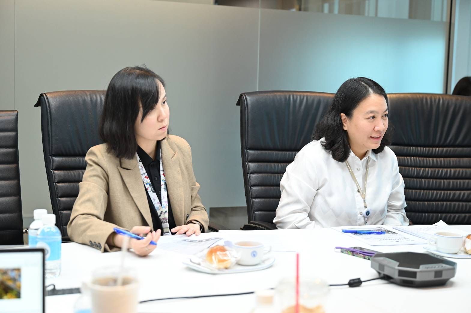 Two professional women attending a meeting at a conference table, observing a discussion.