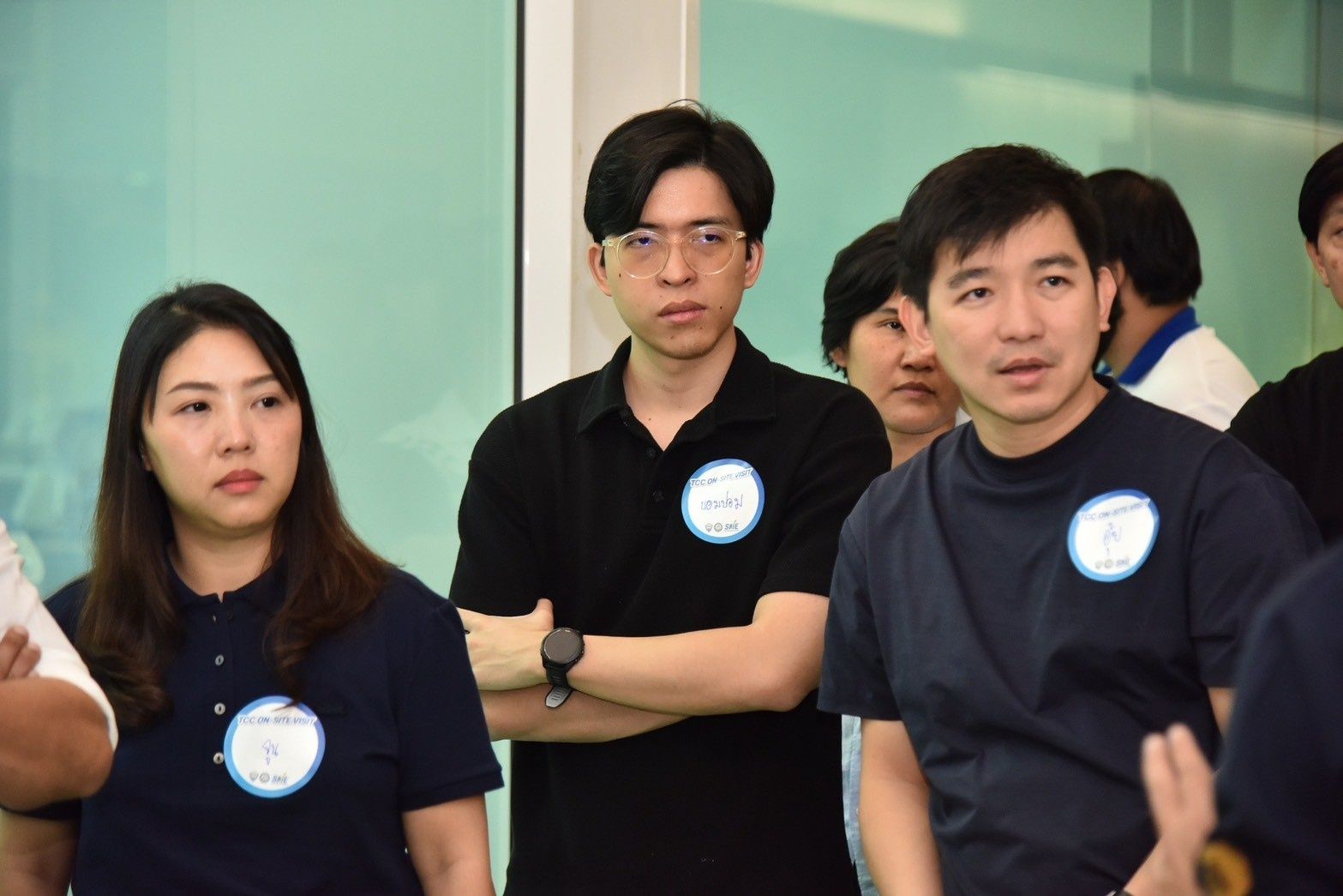 Three Asian people, two women and one man, stand with badges in a group setting.