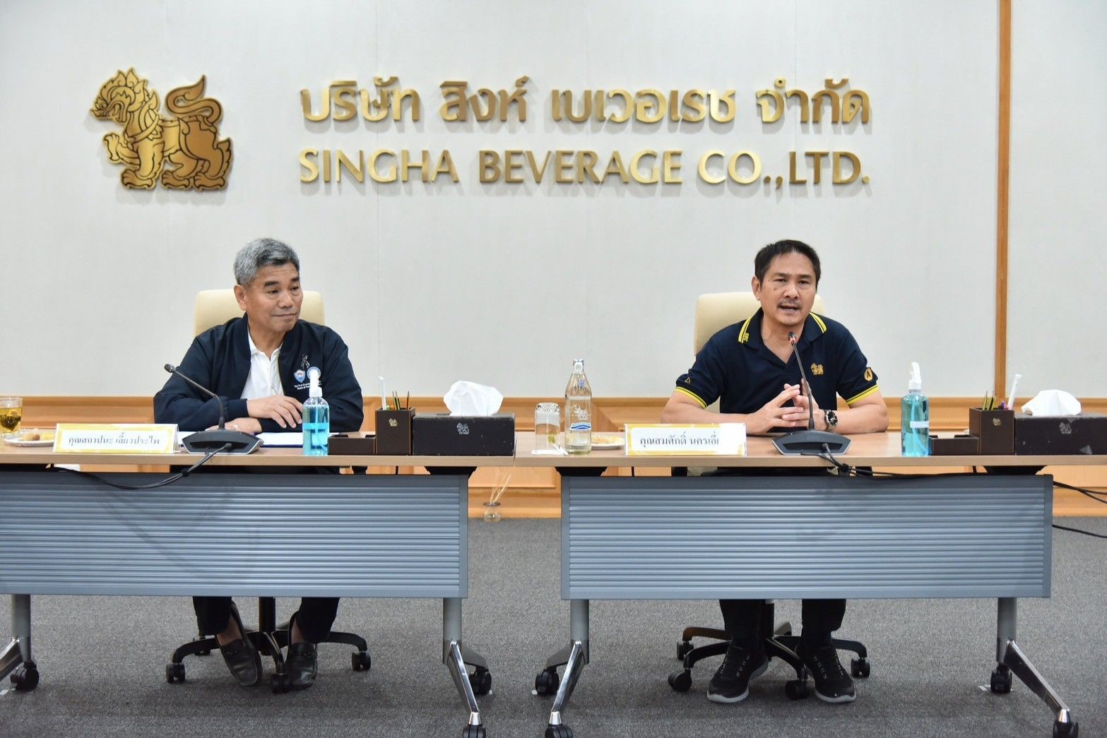 Two men at a meeting table with "SINGHA BEVERAGE CO.,LTD." text in the background.