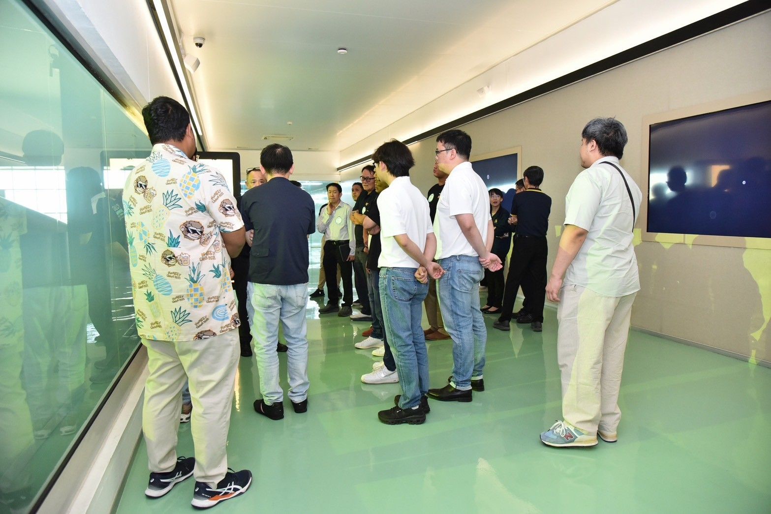 Group of people in a modern hallway observing interactive displays on the wall.