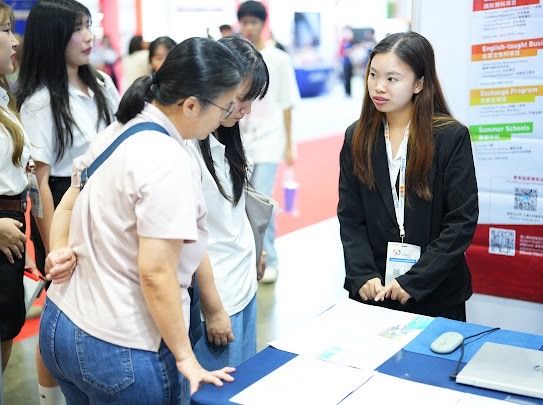 Young professional woman advises two students at a recruitment or information booth.