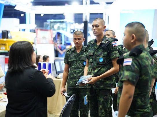 Thai soldiers in uniform stand at an exhibition booth, interacting with a civilian woman.