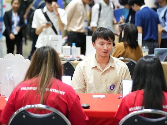 Young man in a light shirt speaks with two people in red shirts at a table.