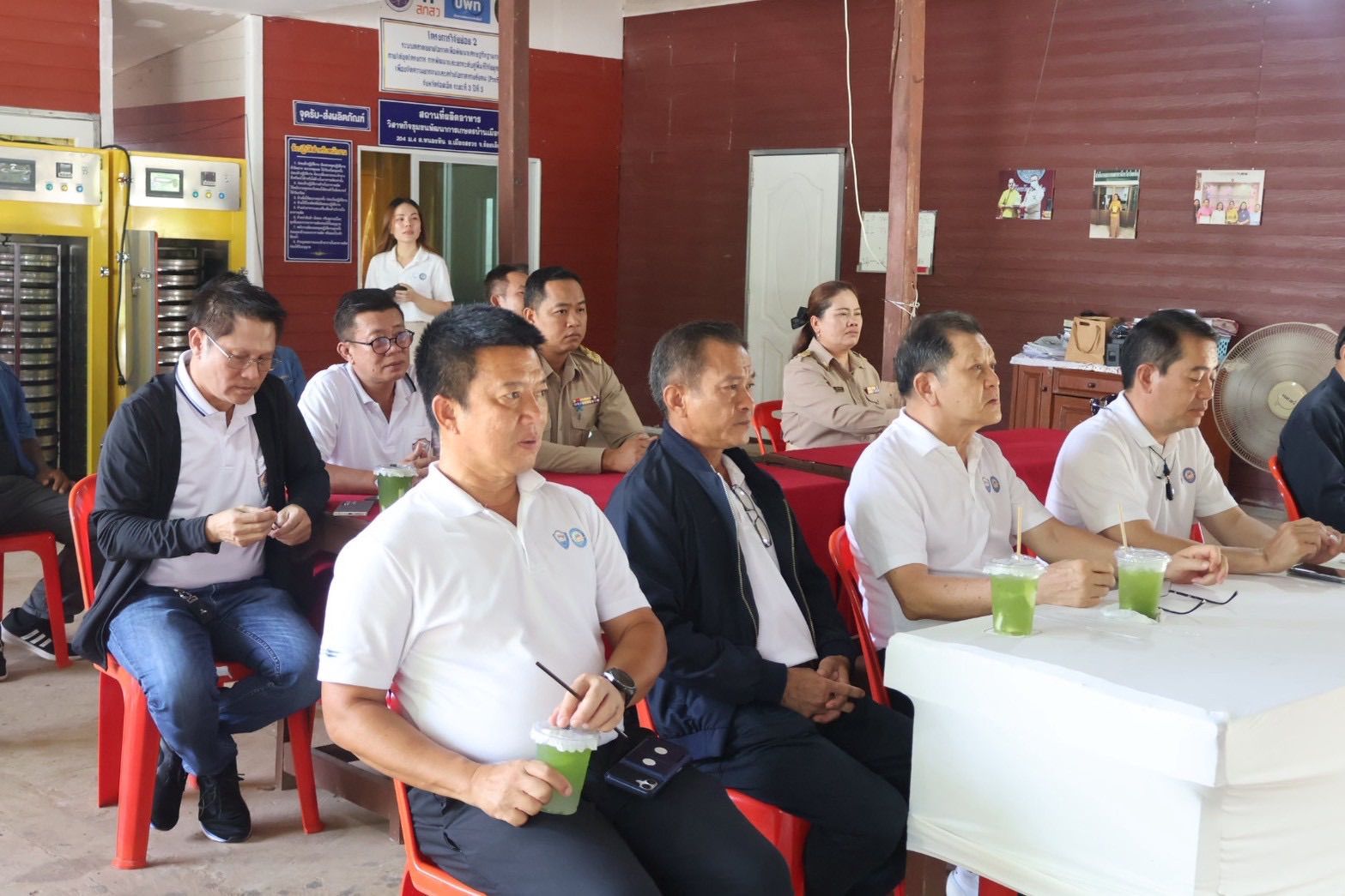 A group of men and women attend an indoor meeting, seated at tables with drinks.