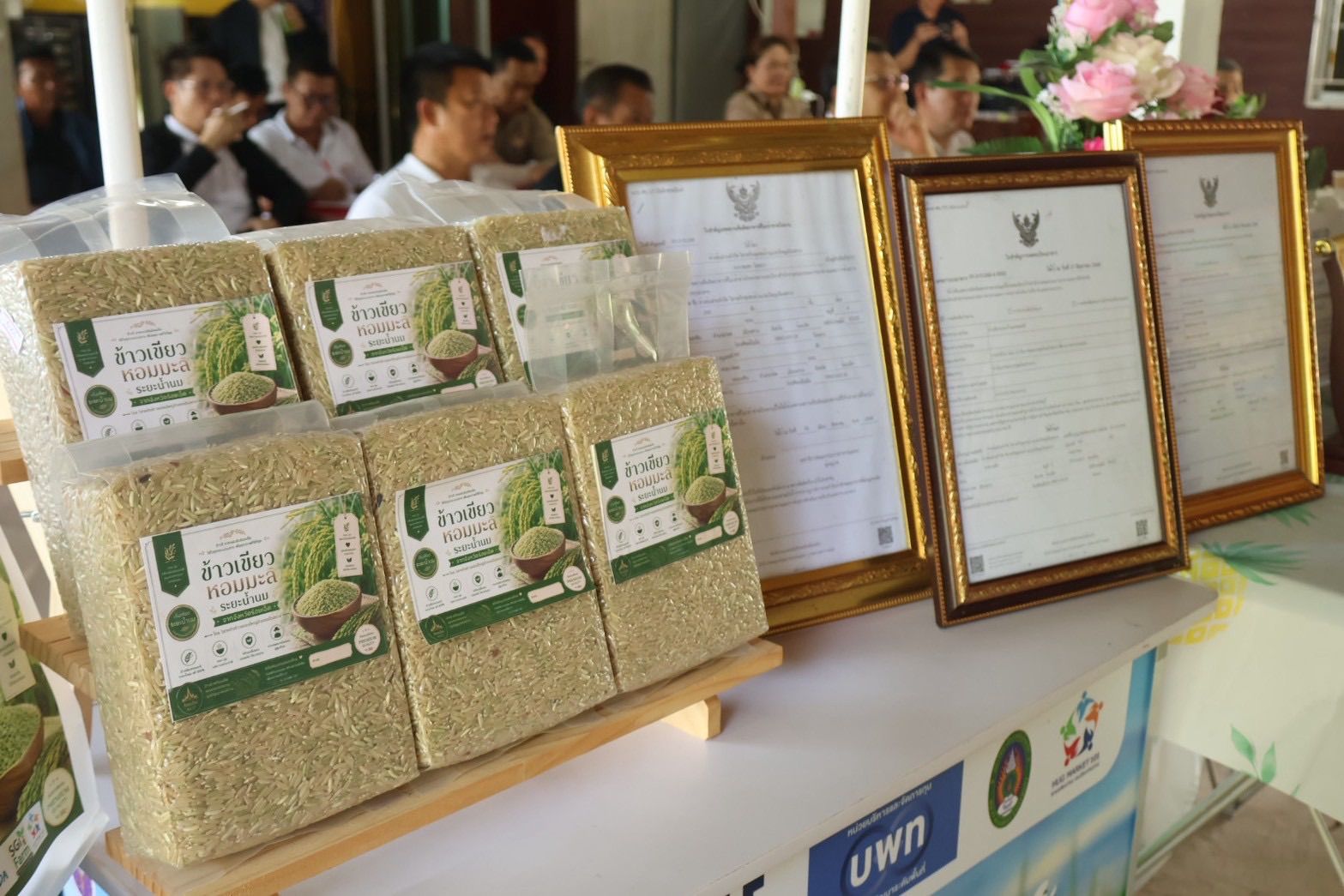 Packages of grain on a wooden display stand next to framed certificates at an event.