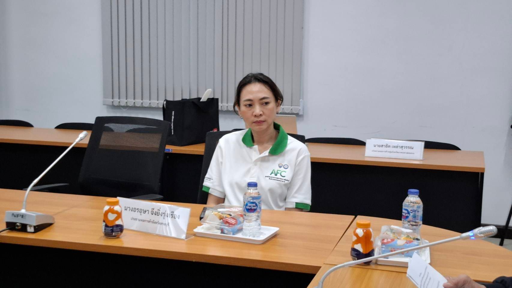Woman in white and green polo shirt sitting at a conference table.