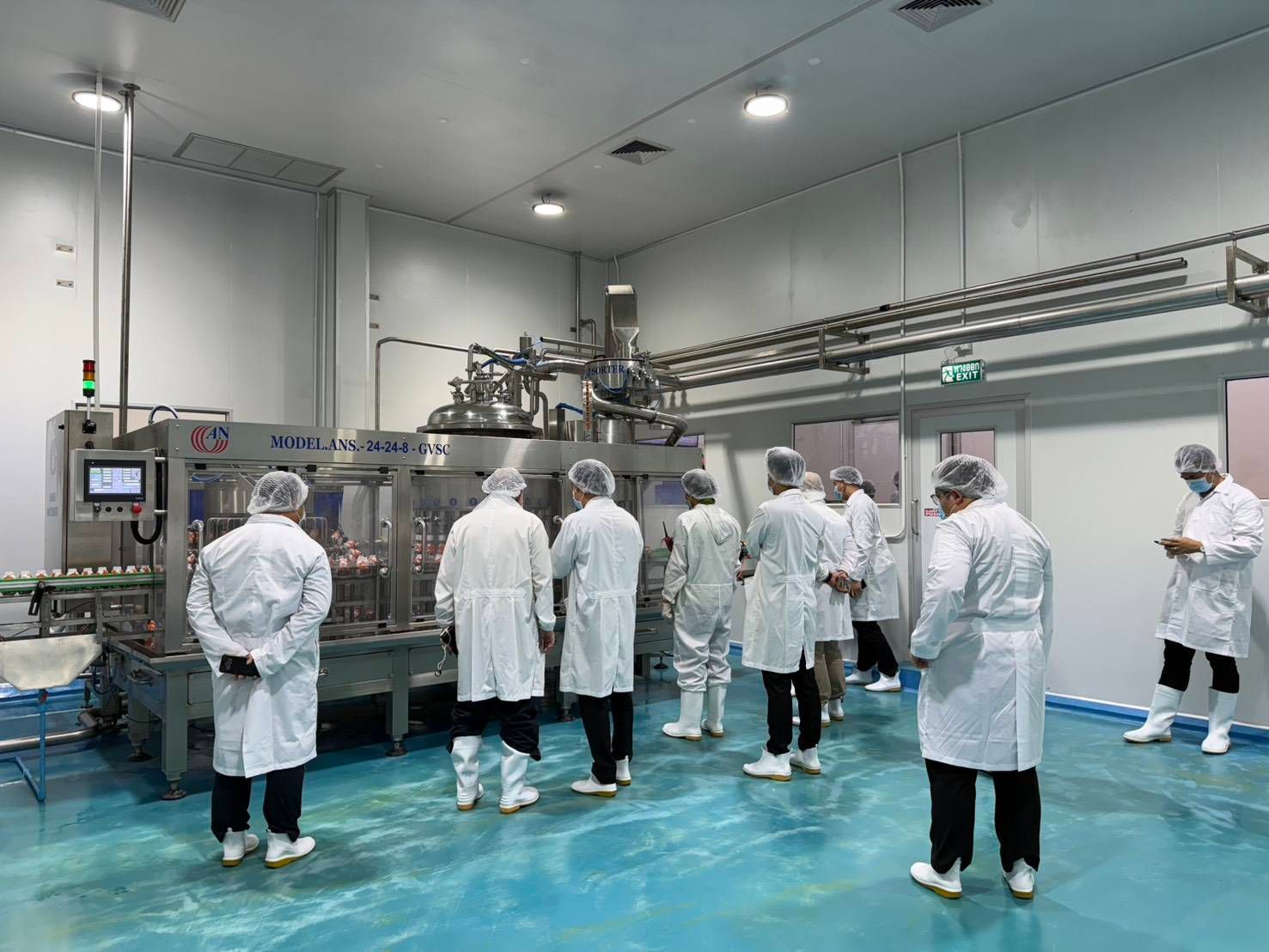People in lab coats and hairnets observe industrial machinery in a clean room facility.