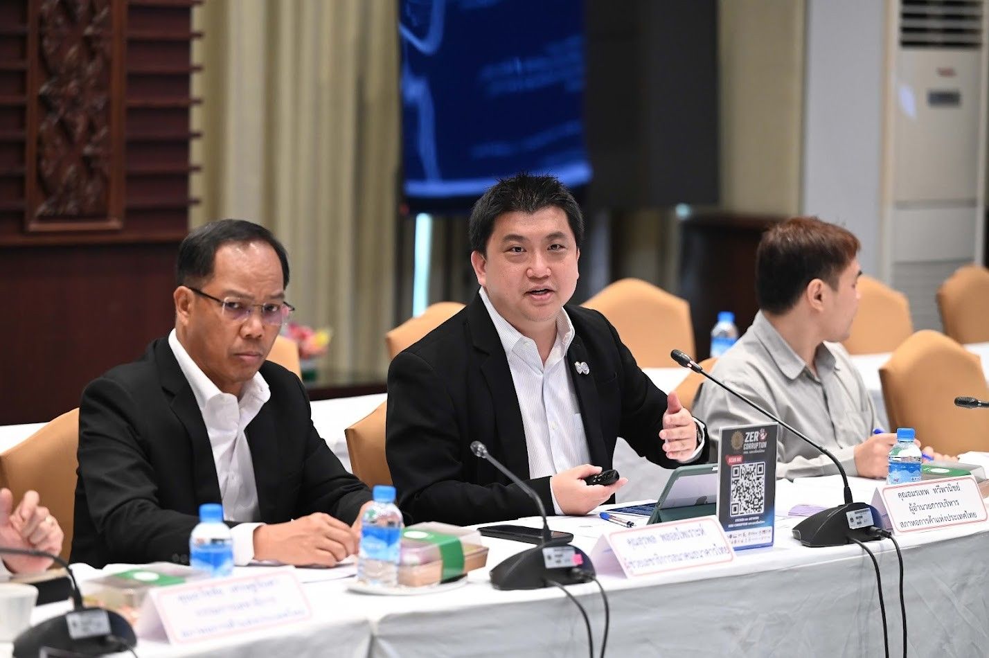 Three men at a conference table, with one speaker gesturing during a discussion.