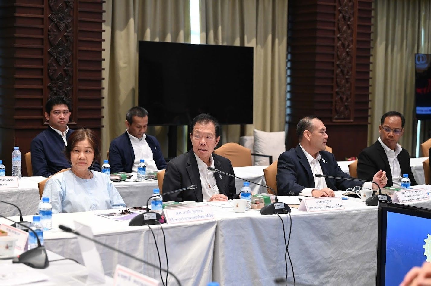 People attending a formal business meeting around a large conference table.