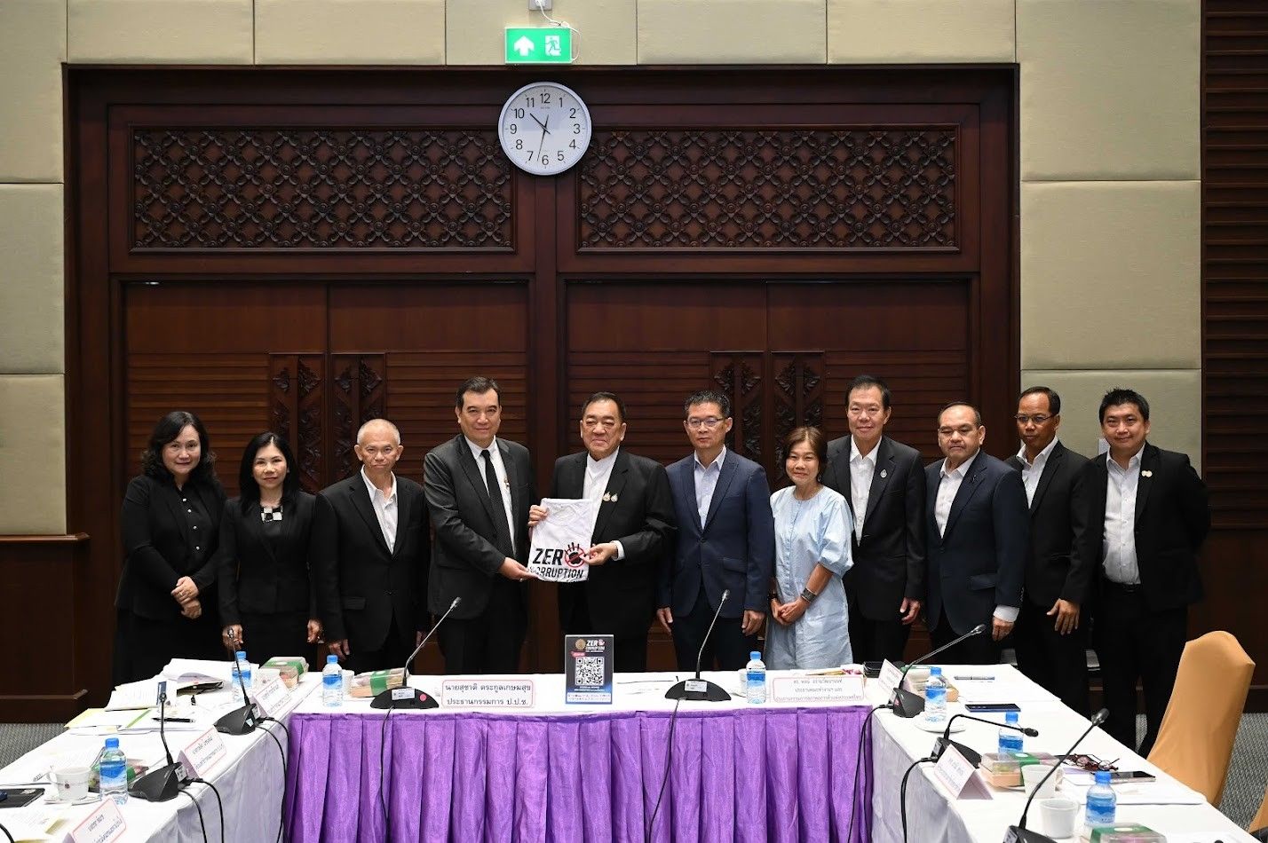 Business professionals shaking hands and exchanging documents in a formal meeting room.