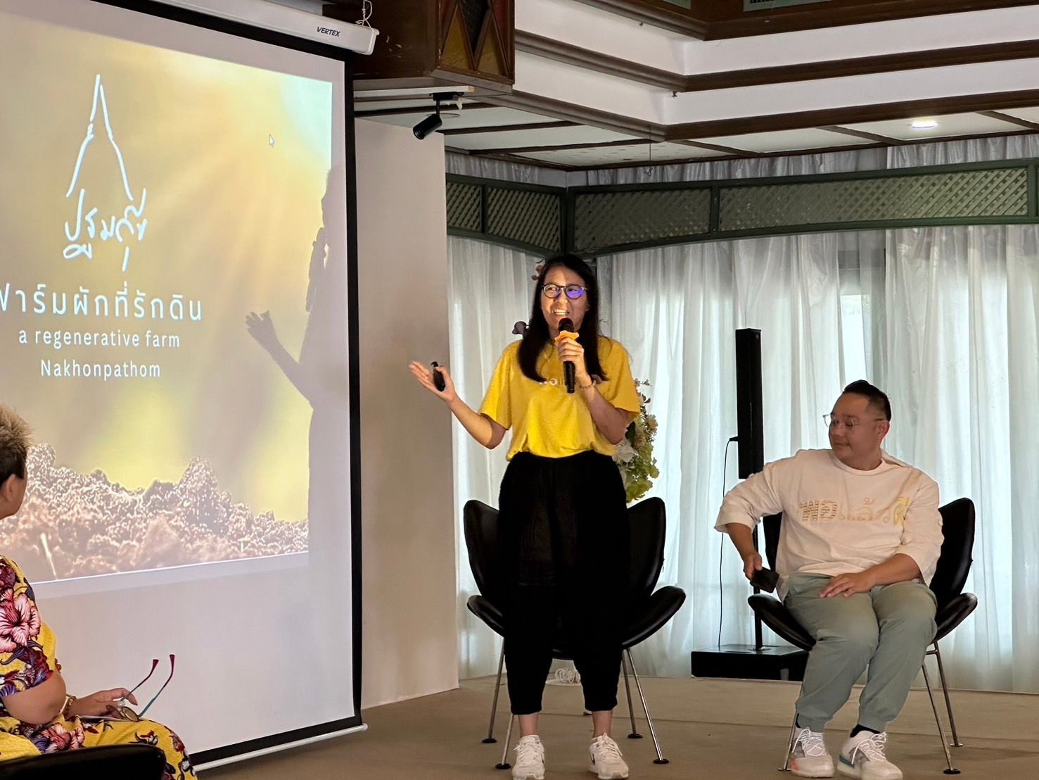 Woman in yellow shirt speaking at a presentation with a projected golden graphic.