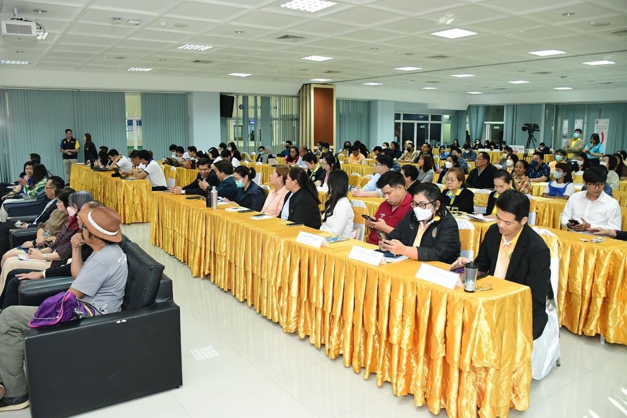 Attendees sit at yellow-draped tables in a well-lit conference room.