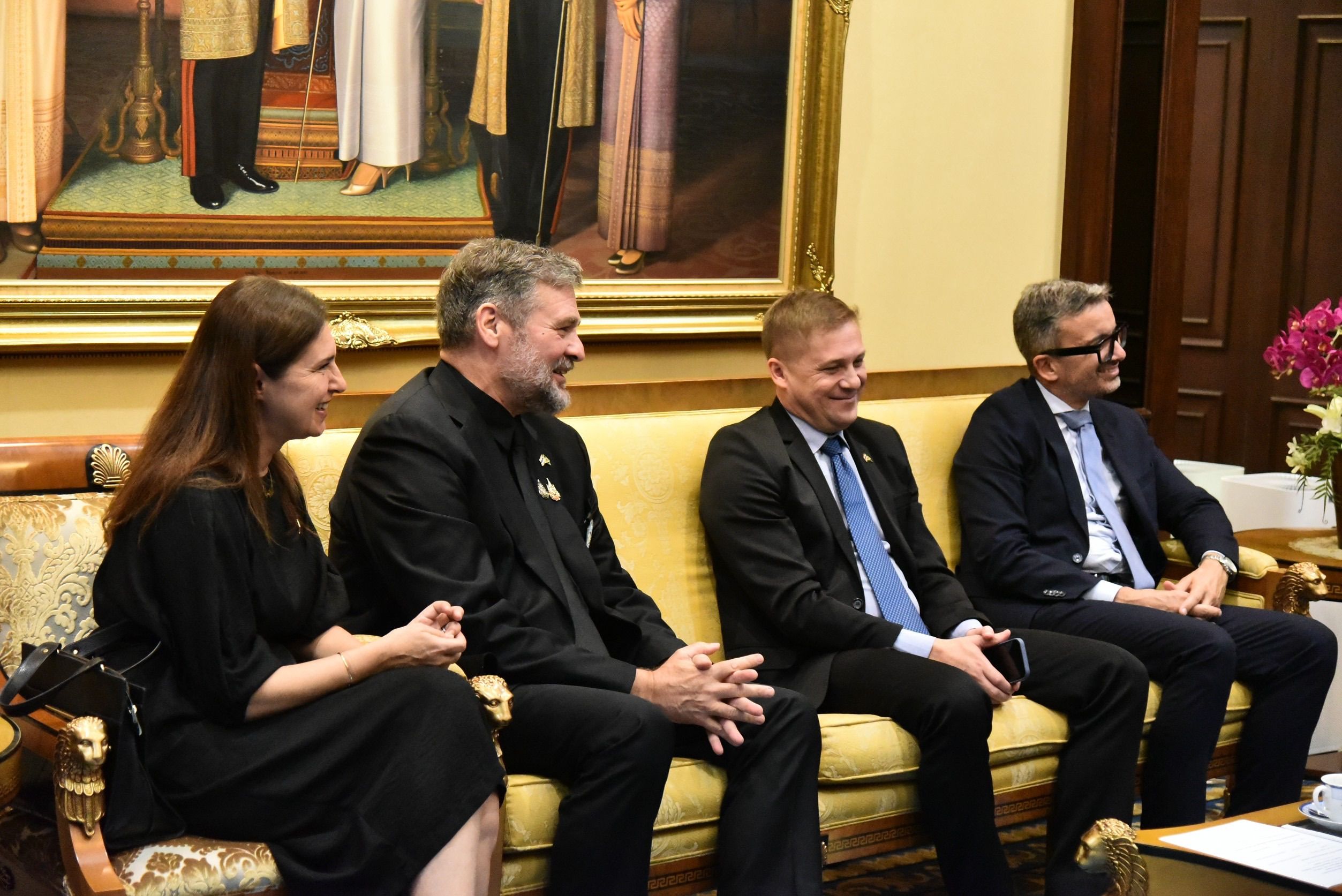 Four people, including two men in suits, smiling and conversing in a formal setting.