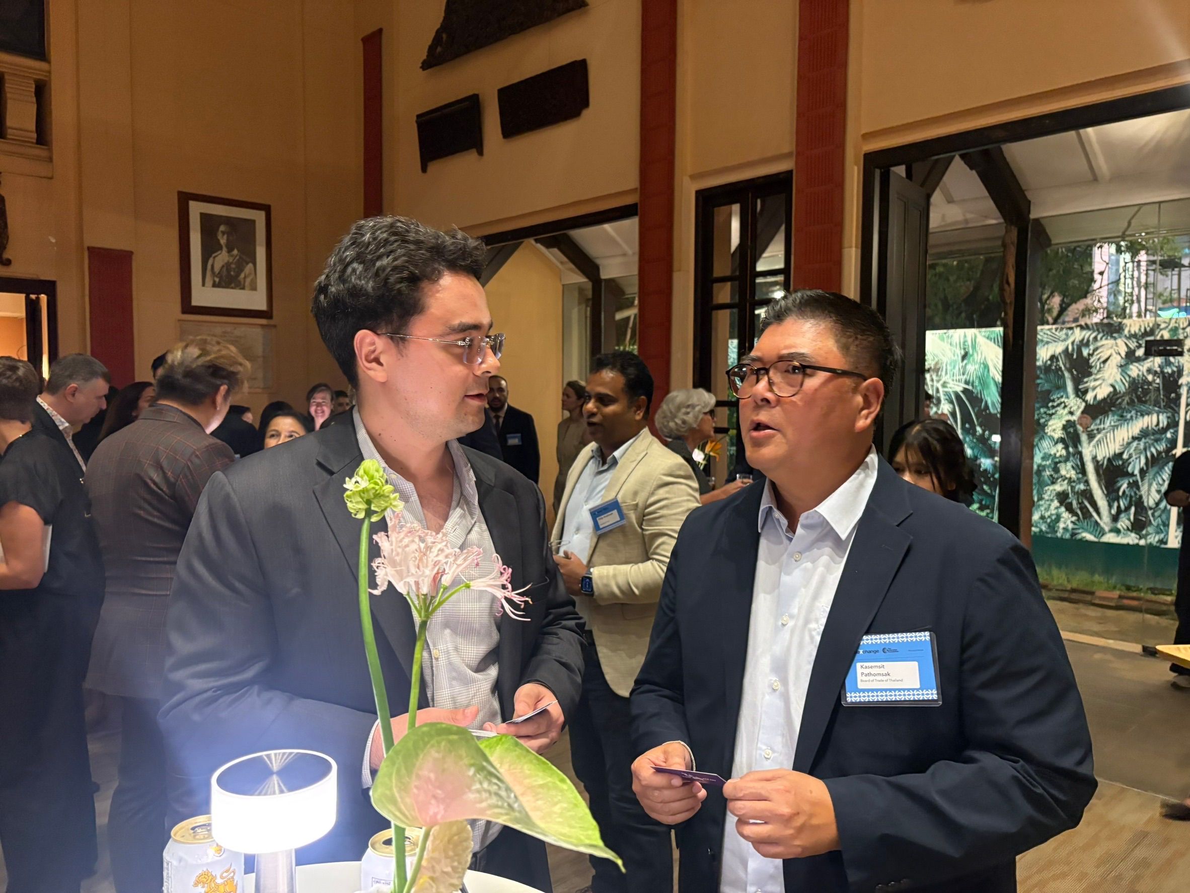 Two professionals engage in conversation at an indoor event, with a floral arrangement between them.