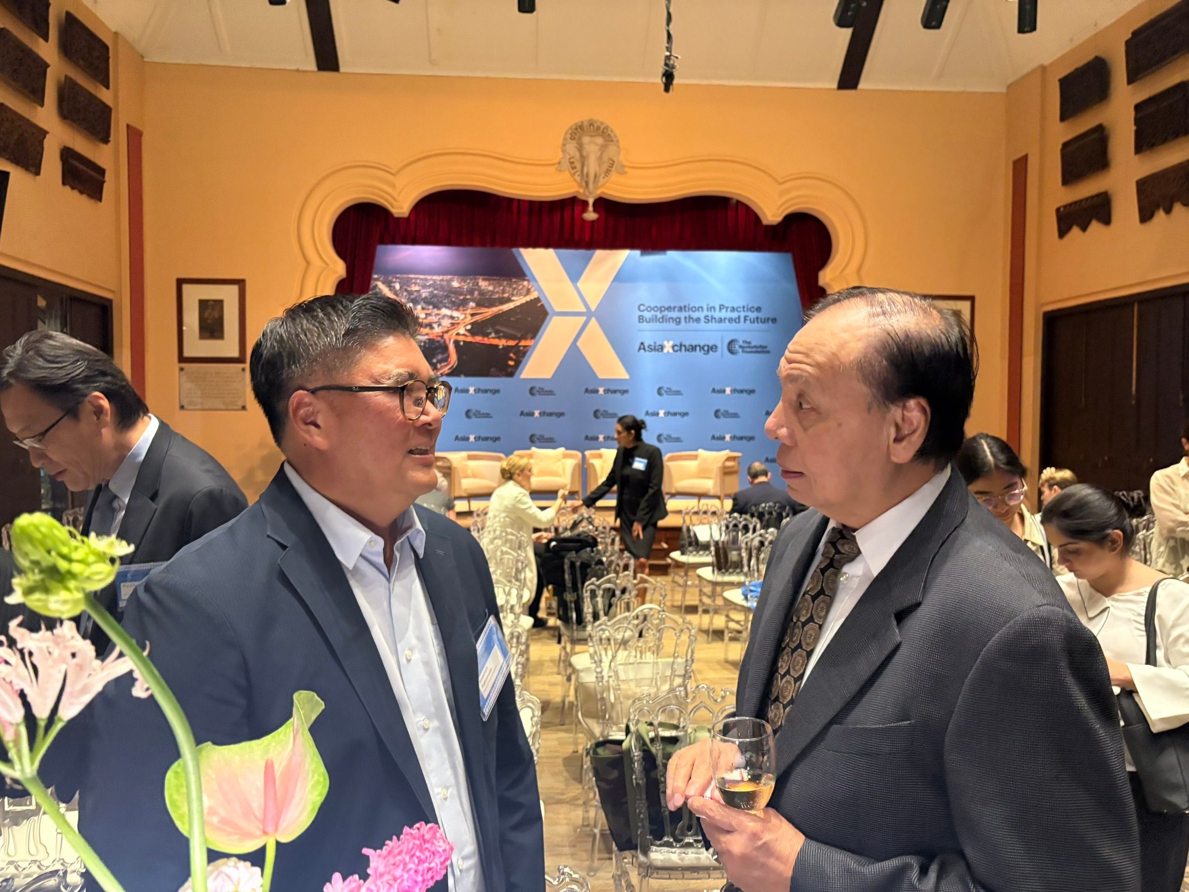 Two men in suits engage in conversation at a professional indoor event.