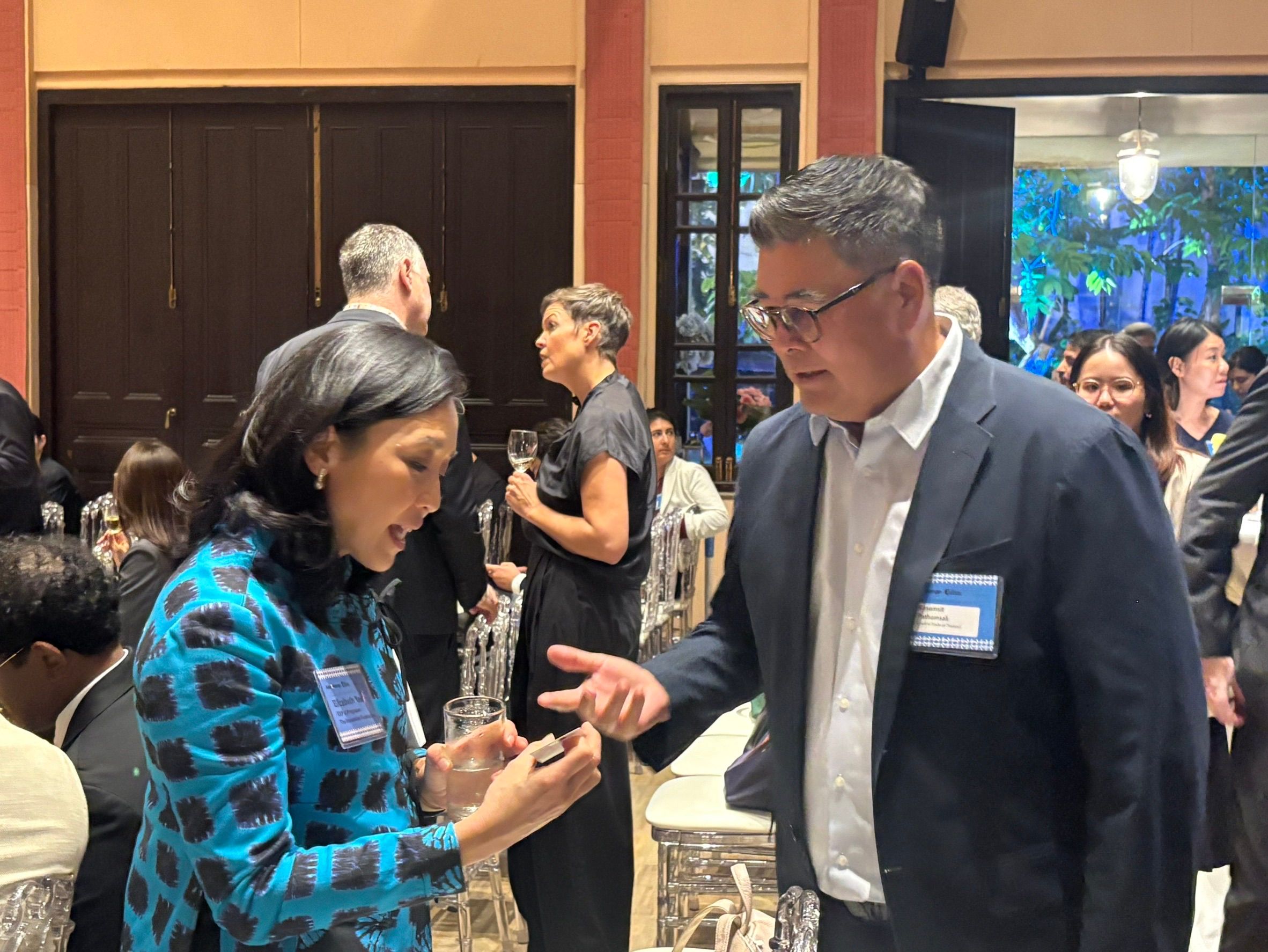 Woman in blue jacket engages with man in suit at a busy indoor networking event.