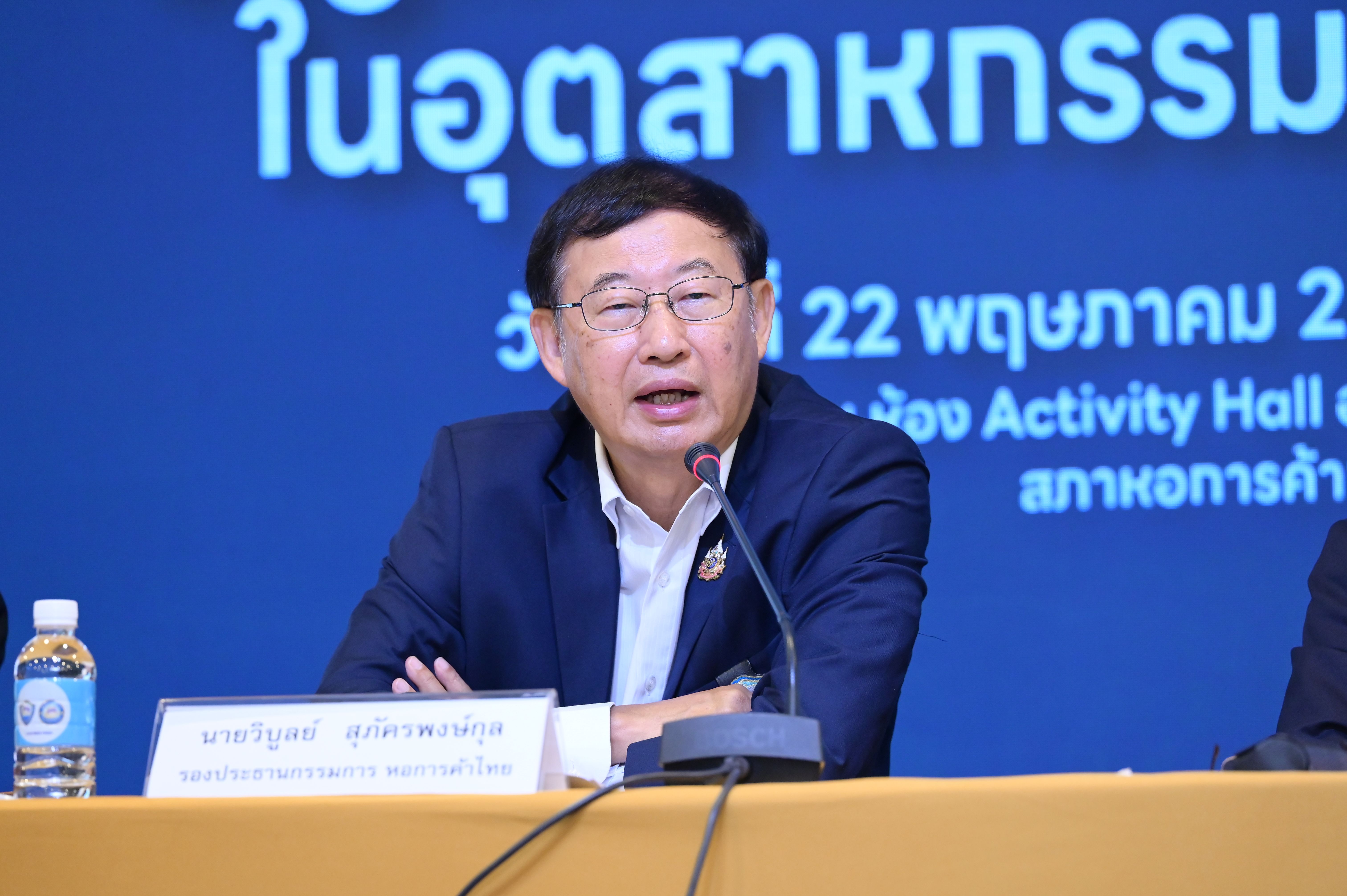 Man in glasses and blue suit speaks at podium during a conference.