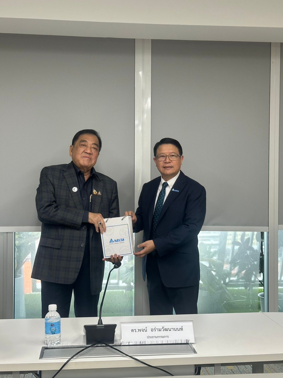 Two business professionals in suits exchange a document during a formal meeting.