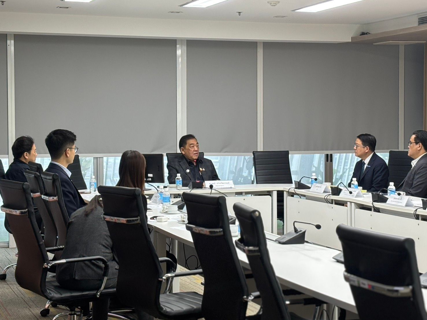 Professionals in business attire are engaged in a meeting around a large conference table.