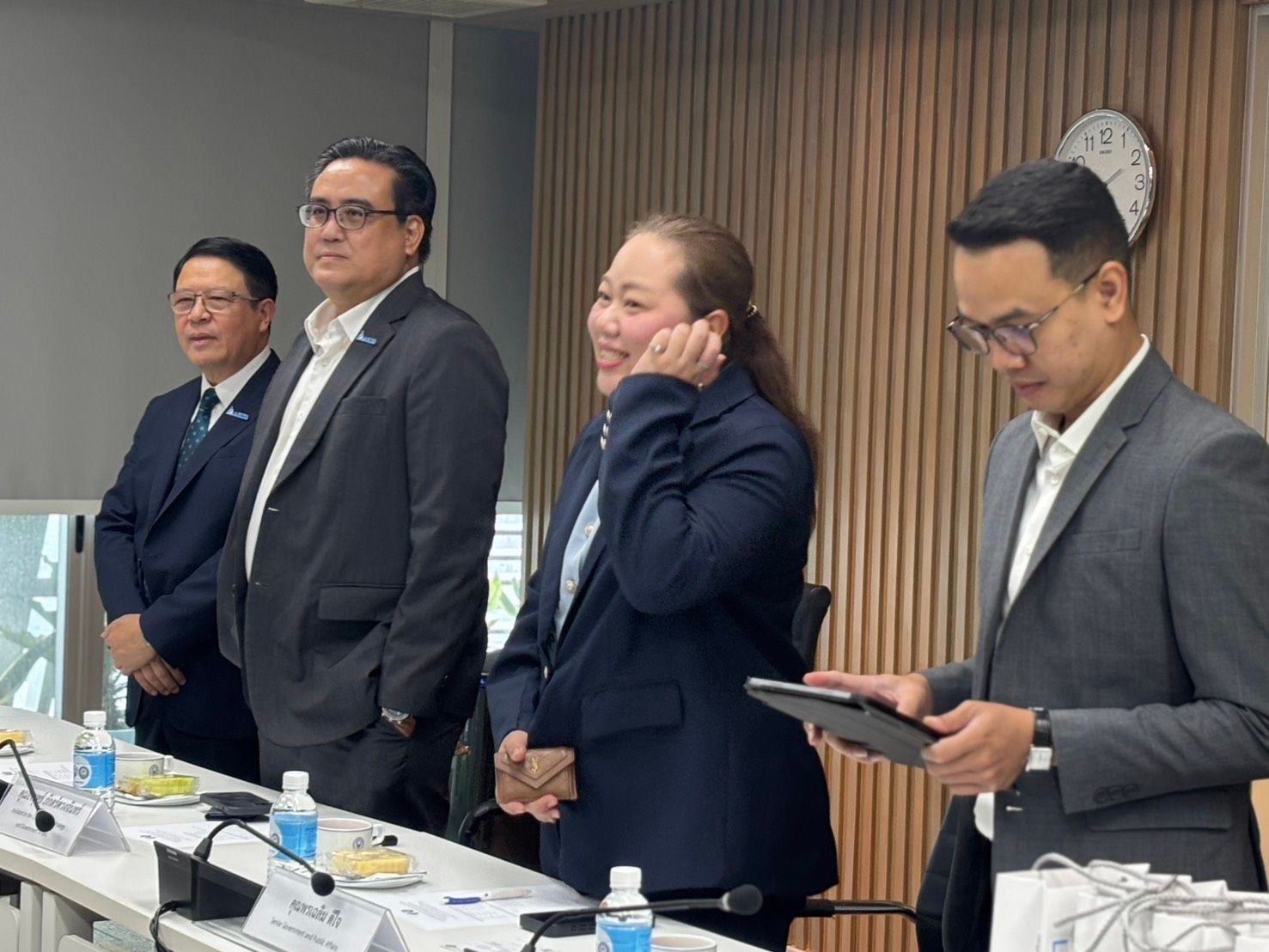 Four professionals standing in a modern meeting room, one woman smiling brightly.