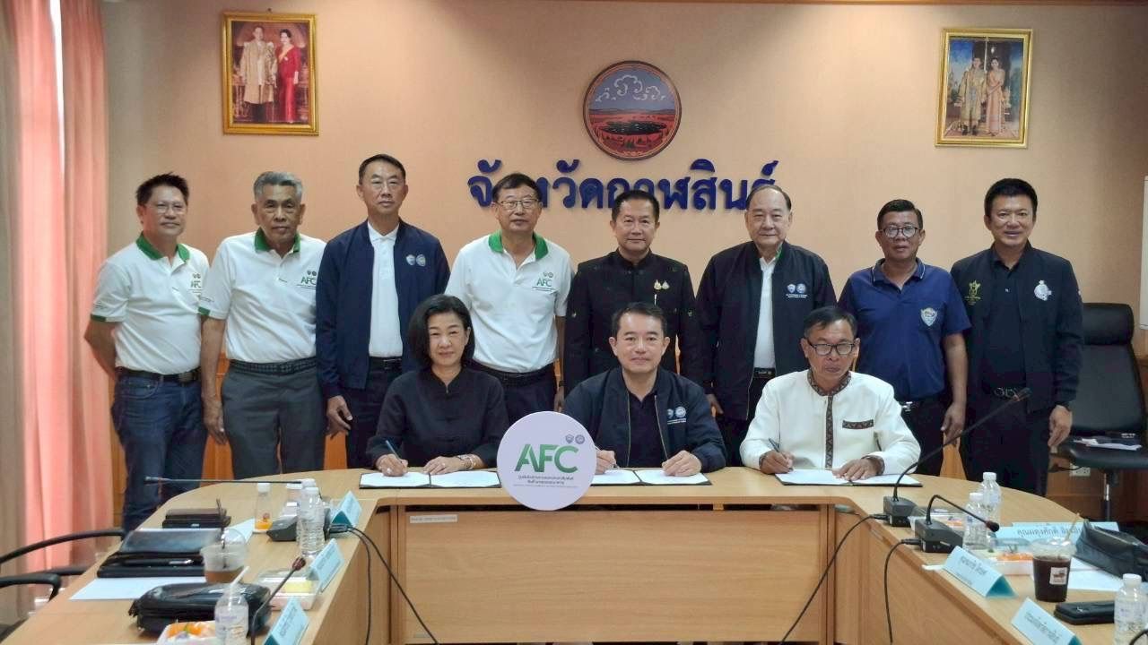 A group of eleven Thai officials, mostly men, stand and sit around a meeting table.