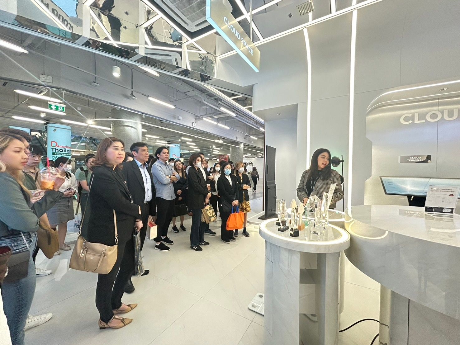 A woman speaks to a diverse group of people in a modern, brightly lit retail space.