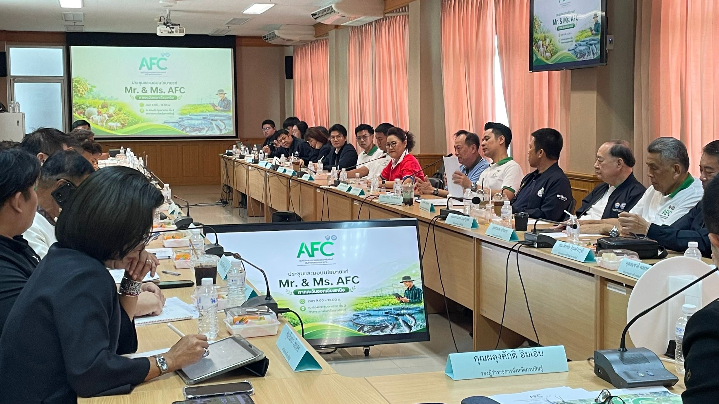 Professionals attend a meeting with two screens displaying 'AFC' presentation.