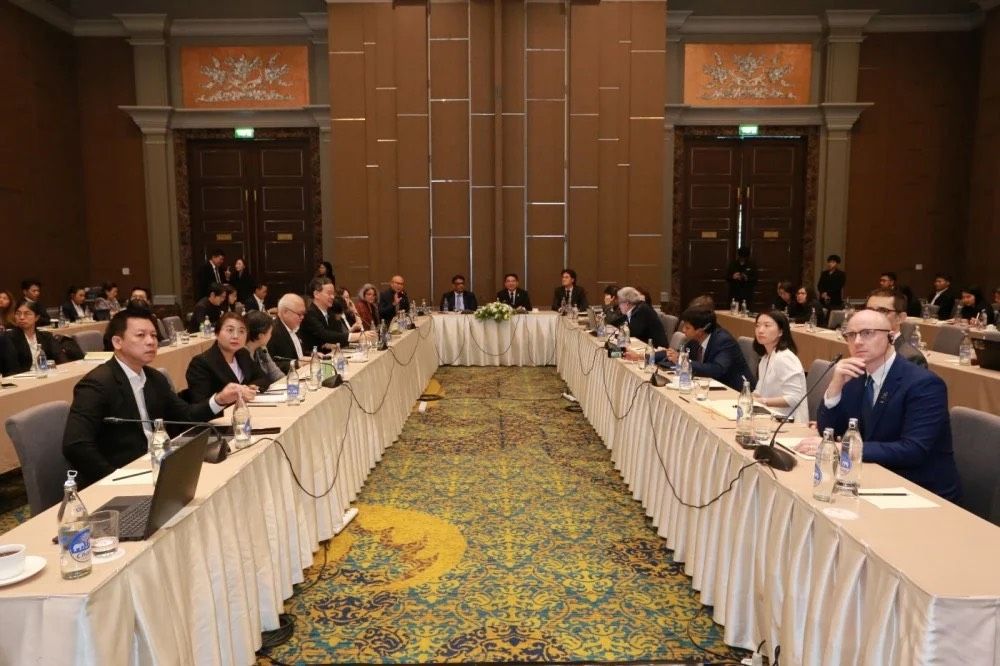 Attendees seated around a large U-shaped table in a formal conference room setting.