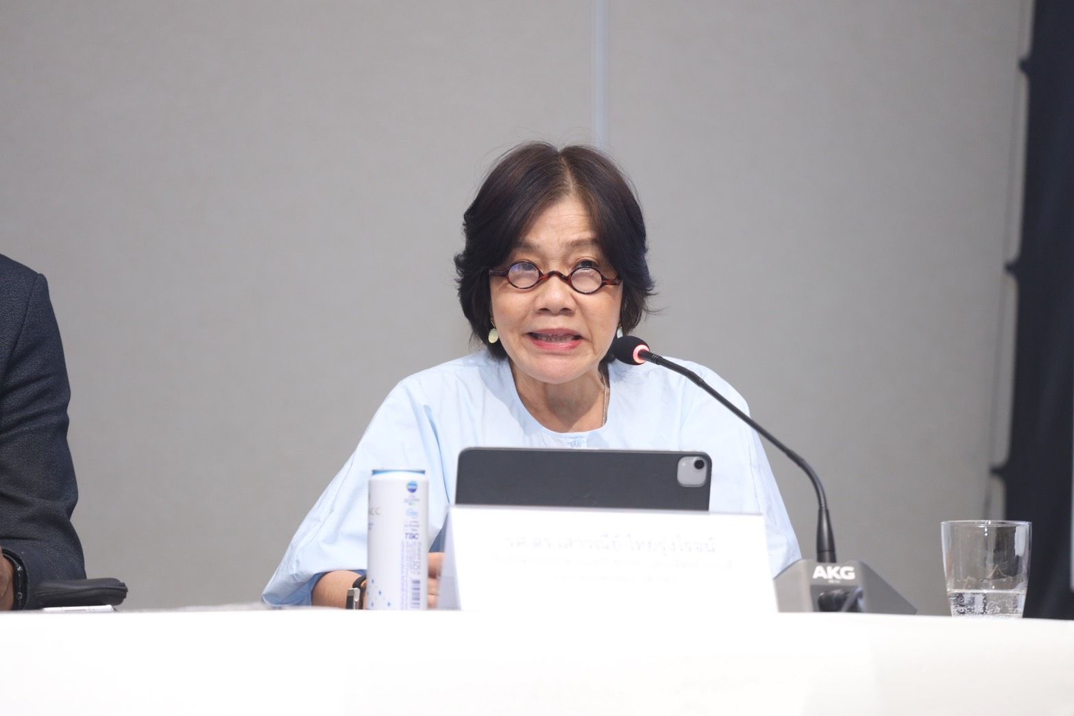 Woman with short dark hair and glasses speaking into a microphone at a table.